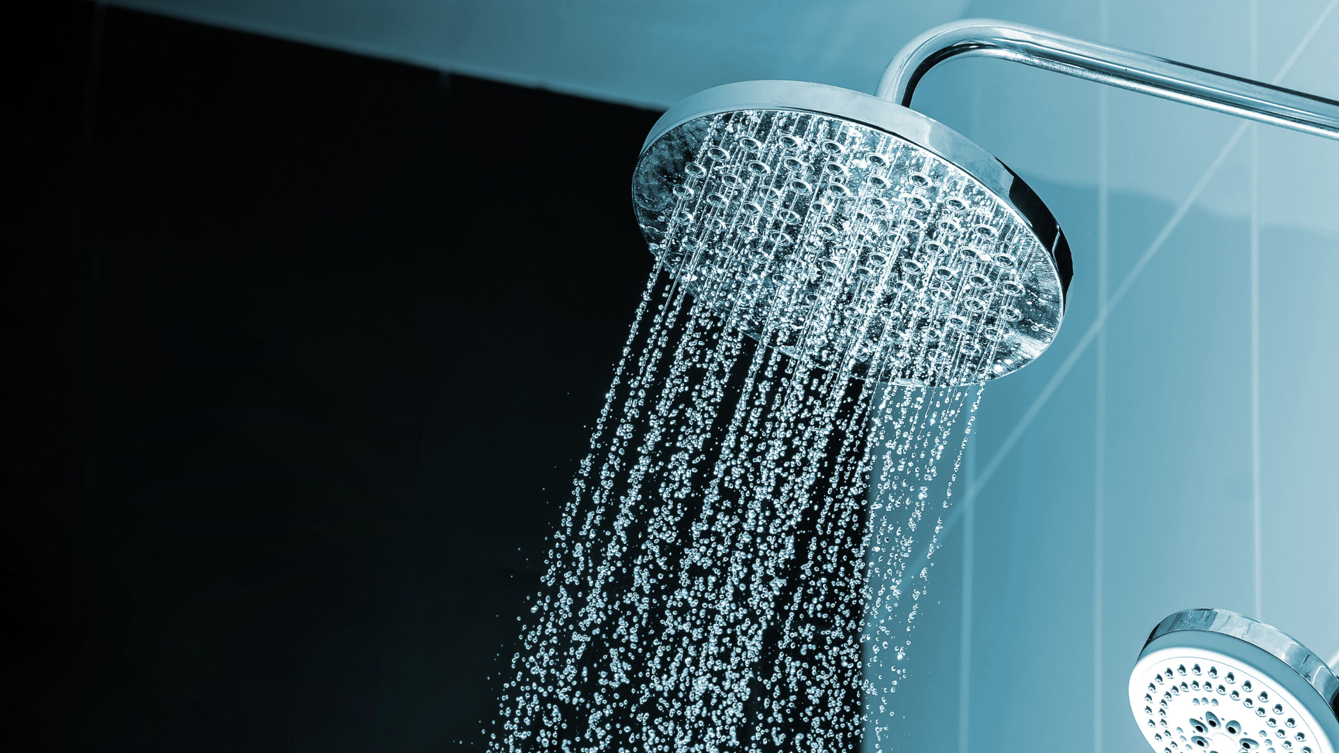 Duschkopf, der einen Wasserstrahl in einem Badezimmer mit einer dunkel gefliesten Wand im Hintergrund freigibt.