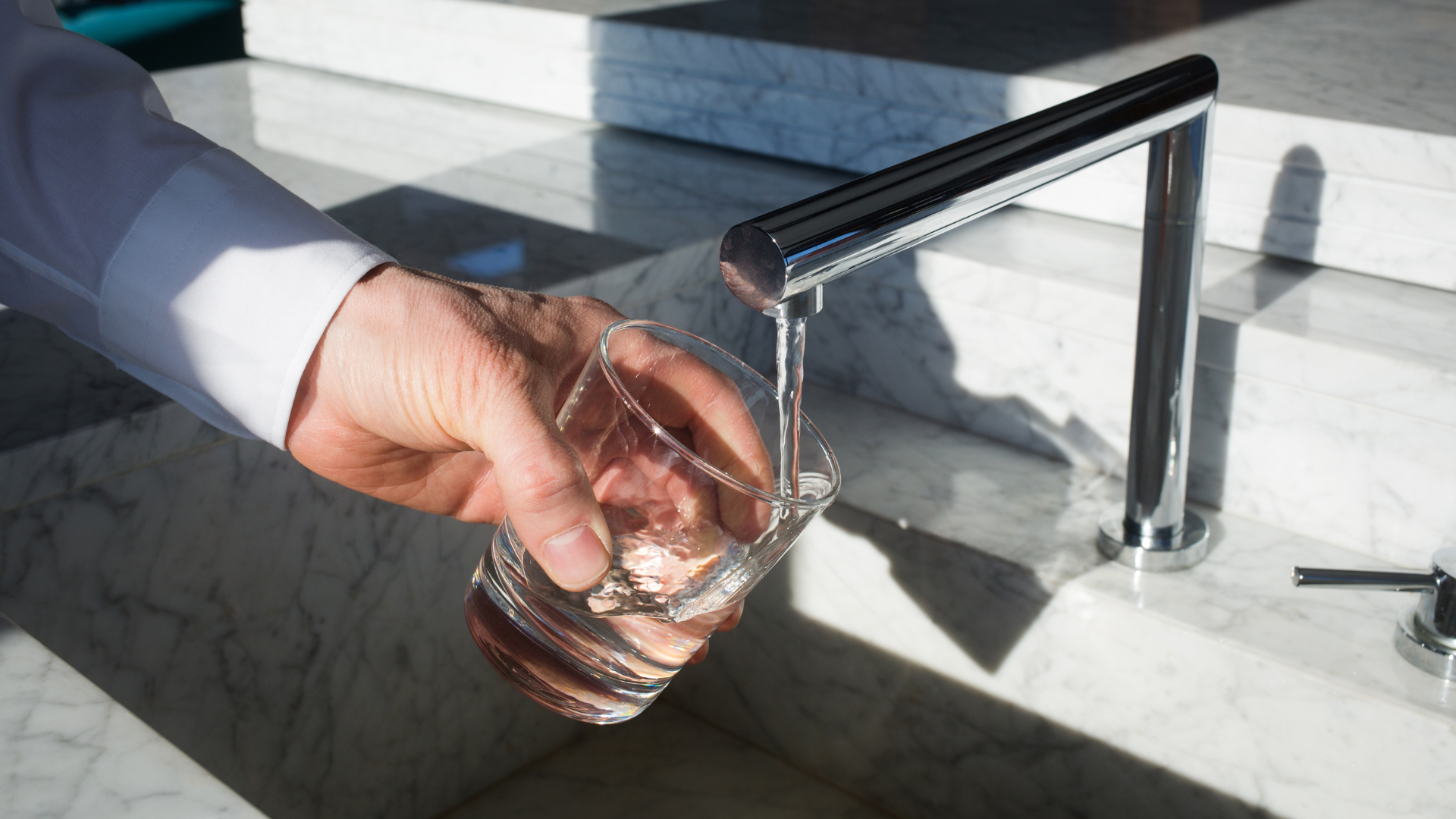 Eine Person füllt ein Glas mit Wasser aus einem modernen Wasserhahn über einem Marmorwaschbecken.