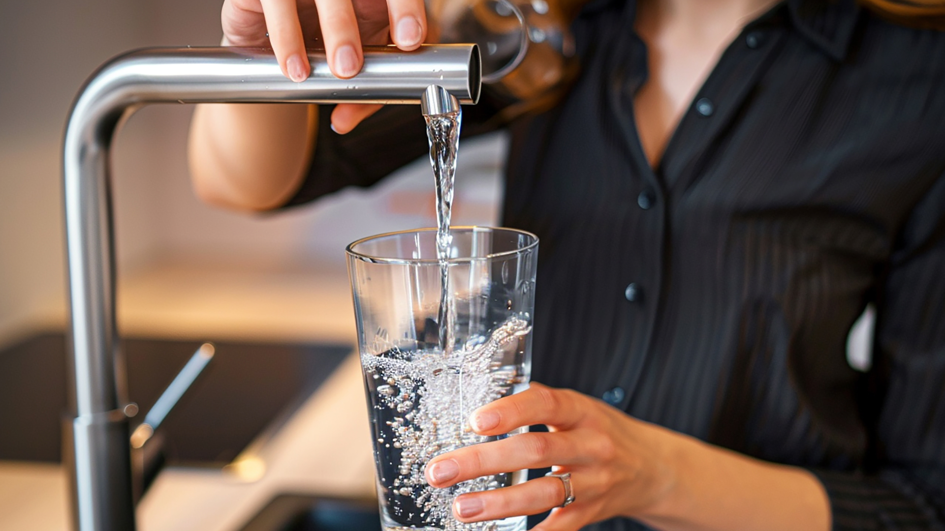 Ein Kind füllt eine Plastikflasche mit Wasser aus einem Küchenhahn.