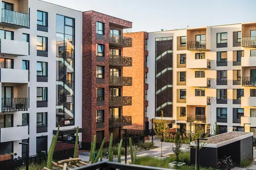 Moderne Apartmentgebäude mit Balkonen und einer Mischung aus weißen, beigen und Backsteinfassaden, umgeben von grüner Landschaft unter klarem Himmel.