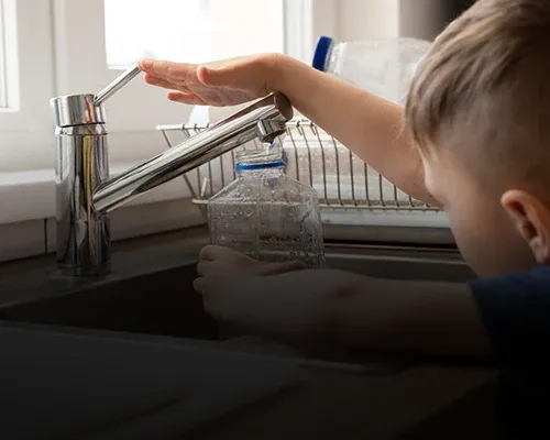Ein Kind füllt eine Plastikflasche mit Wasser aus einem Küchenhahn.