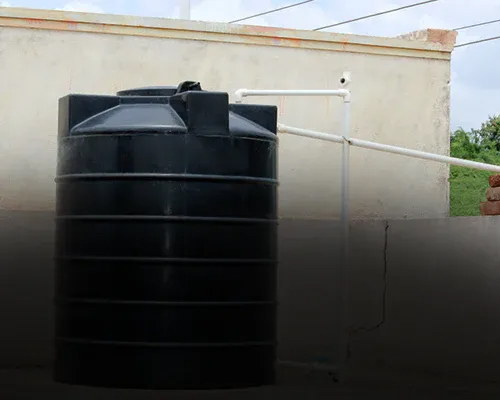 Ein großer, schwarzer, zylindrischer Wassertank im Freien mit weißen Rohren, die mit einer beigen Wand im Hintergrund verbunden sind.